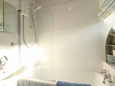 A bathroom with a bathtub shower combination a sink with a faucet a mirror and a small boat-shaped shelf at Timbers in Weybourne