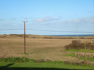 A field with a utility pole and wires and a body of water in the distance at Timbers in Weybourne