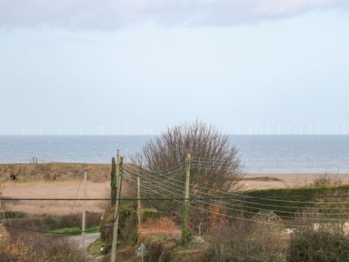 A coastal landscape with power lines trees and wind turbines in the sea at Timbers in Weybourne