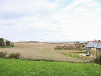 A field with a house on the right and the sea in the background at Timbers in Weybourne