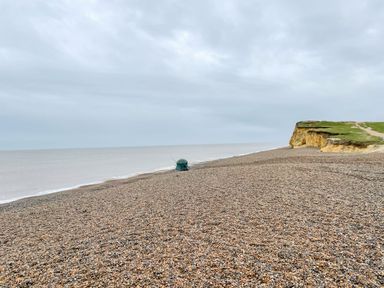 A pebble beach with a green tent near the shoreline and cliffs to the right at Timbers Weybourne