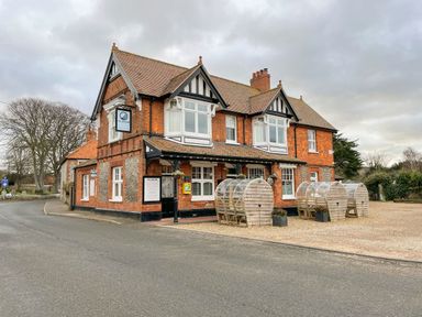 A two-story brick building with outdoor wooden pods by a road at Timbers in Weybourne