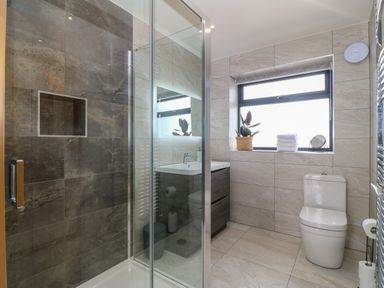A bathroom with a glass shower enclosure a toilet a sink with cabinet and a window with towels and a plant on the sill at Refail Fach Near Cemaes Bay