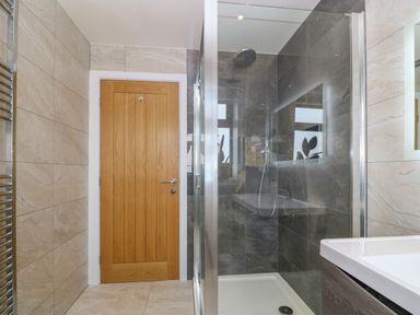 A bathroom with a wooden door a glass shower enclosure and a white sink at Refail Fach Near Cemaes Bay