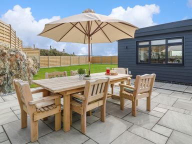 An outdoor patio with wooden table and chairs under umbrella next to a dark exterior building at Refail Fach Near Cemaes Bay