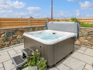 An outdoor hot tub with steps next to it and plants in pots on a stone patio at Refail Fach Near Cemaes Bay