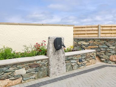 An outdoor area with stone walls a flower bed and a mounted electric vehicle charging station at Refail Fach Near Cemaes Bay