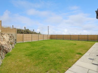 A fenced backyard with a grassy lawn and stone patio at Refail Fach Near Cemaes Bay