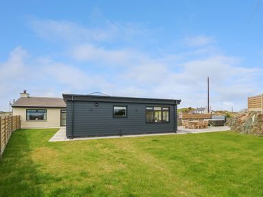 A backyard with a lawn area a patio with outdoor dining furniture and a hot tub at Refail Fach Near Cemaes Bay