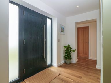 An entryway with a black front door wooden flooring a brown mat a plant in a pot and a closed wooden interior door at Refail Fach Near Cemaes Bay