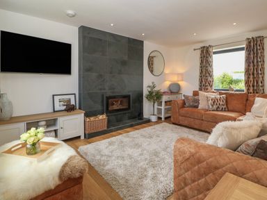 A living room with a fireplace a large rug and brown sofas at Refail Fach Near Cemaes Bay