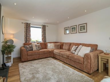 A living room with a large brown sectional sofa cushions patterned curtains and framed pictures on the wall at Refail Fach Near Cemaes Bay