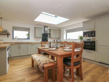A kitchen with grey cabinets a wooden dining table with plates and glasses and a skylight at Refail Fach Near Cemaes Bay