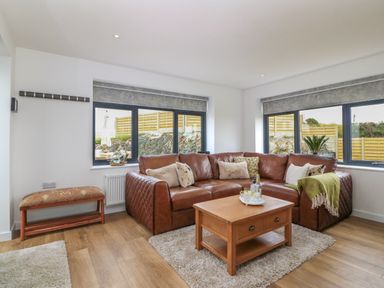A living room with a brown leather corner sofa a wooden coffee table and windows showing a fenced garden at Refail Fach Near Cemaes Bay