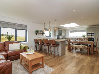 An open plan living area with brown leather sofas a wooden coffee table and a kitchen island with wooden bar stools at Refail Fach Near Cemaes Bay