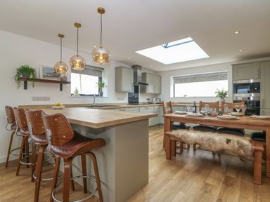 A kitchen with a wooden island and bar stools and a dining table set with plates and glasses at Refail Fach Near Cemaes Bay