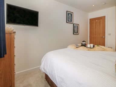A bedroom with a bed covered in white bedding a wooden door and cornices a wall-mounted TV and two framed pictures near Refail Fach Near Cemaes Bay