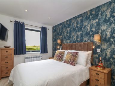 A bedroom with a bed two bedside tables a chest of drawers and a window with blue curtains at Refail Fach Near Cemaes Bay