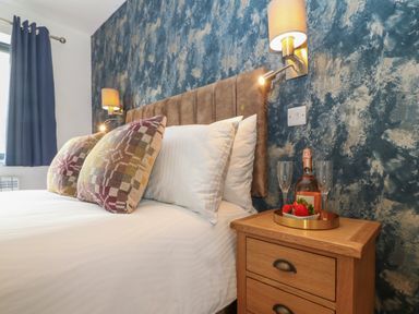 A bedroom with a bed with pillows beside a wooden nightstand with a bottle and glasses on a tray at Refail Fach Near Cemaes Bay