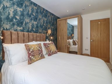 A bedroom with a bed white bedding patterned pillows a textured blue and beige wall a wooden wardrobe with a mirror and a wooden door at Refail Fach Near Cemaes Bay