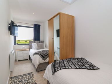 A bedroom with two single beds a wooden wardrobe a nightstand and a wall-mounted TV at Refail Fach Near Cemaes Bay
