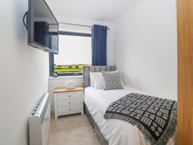 A small bedroom with a bed a bedside table a window with blue curtains and a wall-mounted tv at Refail Fach Near Cemaes Bay