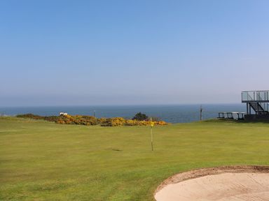 A golf course green with a sand bunker and a yellow flag near the sea at Refail Fach Near Cemaes Bay
