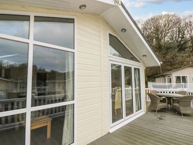 An outdoor deck with a table and four chairs outside a building with large windows and glass doors at Dono's Lodge in Stepaside near Kilgetty Heritage Park
