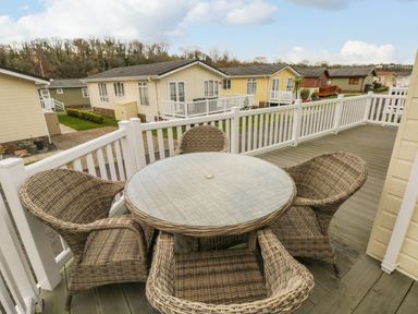 A balcony with a round glass table and four wicker chairs overlooking residential houses at Dono's Lodge in Stepaside near Kilgetty Heritage Park
