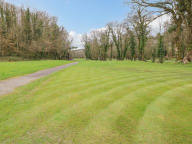 A grass lawn with a narrow gravel path and leafless trees at Dono's Lodge Stepaside near Kilgetty Heritage Park