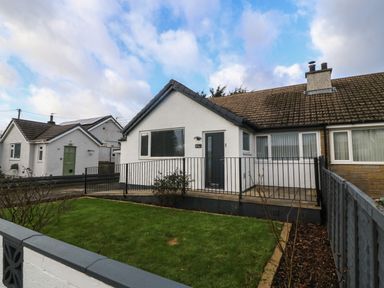 A white semi detached house with a fenced front yard and grass in Llanfairpwllgwyngyll