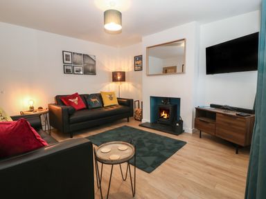 A living room with two black sofas colorful cushions fireplace TV on wooden cabinet and dark rug at Ty Nain in Llanfairpwllgwyngyll