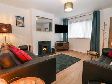 A living room with two black sofas a fireplace a wall mounted tv and a wooden cabinet at Ty Nain in Llanfairpwllgwyngyll