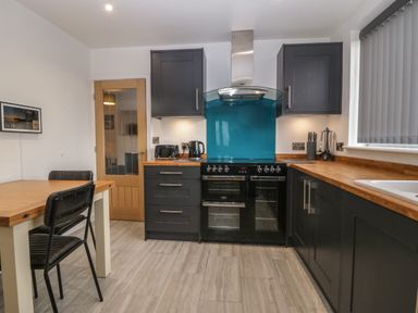 A kitchen with black cabinets wooden countertops a black oven a blue backsplash and a wooden table with black chairs at Ty Nain in Llanfairpwllgwyngyll