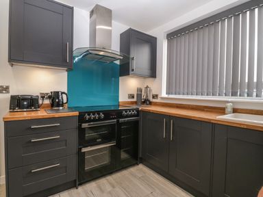 A kitchen with black cabinets wooden countertops a stove toaster kettle knives and utensils at Ty Nain in Llanfairpwllgwyngyll