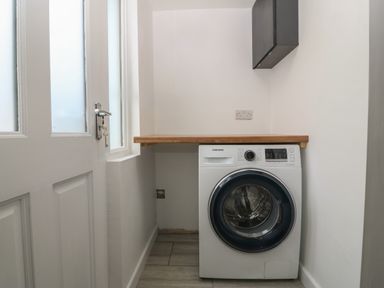 A laundry room with a front-loading washing machine under a wooden countertop at Ty Nain in Llanfairpwllgwyngyll