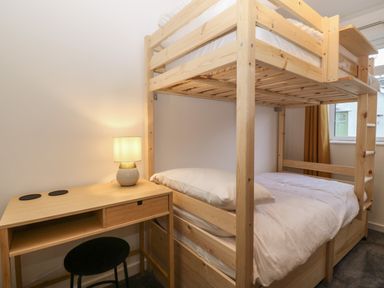 A bedroom with a wooden bunk bed next to a desk with a lamp and a stool at Ty Nain in Llanfairpwllgwyngyll