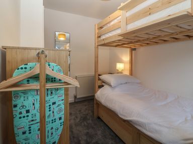 A bedroom with a bunk bed a wooden wardrobe an ironing board and a lamp on a side table at Ty Nain in Llanfairpwllgwyngyll