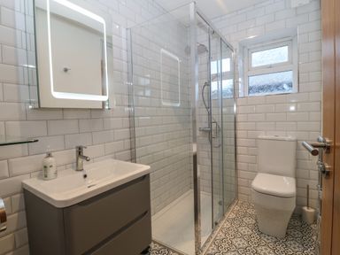 A bathroom with a sink, illuminated mirror, shower enclosure, toilet, and patterned floor tiles at Ty Nain in Llanfairpwllgwyngyll