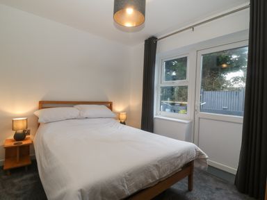 A bedroom with a double bed bedside tables with lamps and a window with curtains at Ty Nain in Llanfairpwllgwyngyll