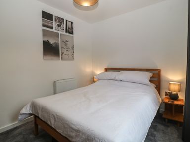 A bedroom with a double bed white bedding bedside table with lamp and wall art at Ty Nain in Llanfairpwllgwyngyll