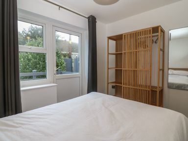A bedroom with a large bed a wooden shelving unit a window and a door with dark curtains at Ty Nain in Llanfairpwllgwyngyll
