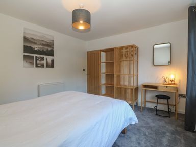 A bedroom with a bed white bedding wooden shelving unit small wooden desk mirror lamp and black stool at Ty Nain in Llanfairpwllgwyngyll