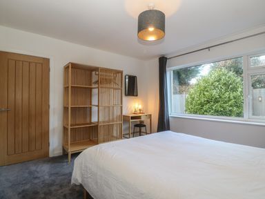 A bedroom with a bed white bedding wooden wardrobe and desk near a large window at Ty Nain in Llanfairpwllgwyngyll