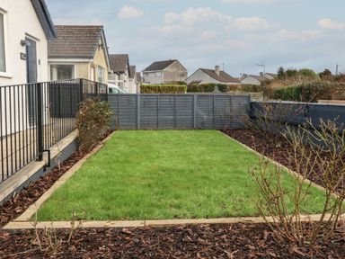 A small fenced garden with grass and plants next to houses at Ty Nain in Llanfairpwllgwyngyll