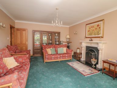 A living room with two red patterned sofas a fireplace with a painting above and a wooden cabinet at Bolger House Ballintubbrid near Kilmuckridge County Wexford