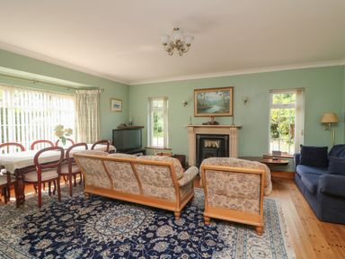 A living room with floral sofas a blue rug a dining table and chairs a fireplace and a television at Bolger House Ballintubbrid near Kilmuckridge County Wexford