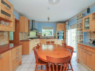 A kitchen with a wooden dining table and chairs light wood cabinets blue walls and striped curtains at Bolger House in Ballintubbrid near Kilmuckridge County Wexford