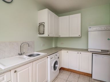A utility room with white cabinets a sink washing machine and dryer at Bolger House Ballintubbrid near Kilmuckridge County Wexford