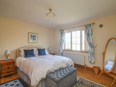 A bedroom with a double bed two bedside tables with lamps a window with curtains and a standing mirror at Bolger House Ballintubbrid near Kilmuckridge County Wexford